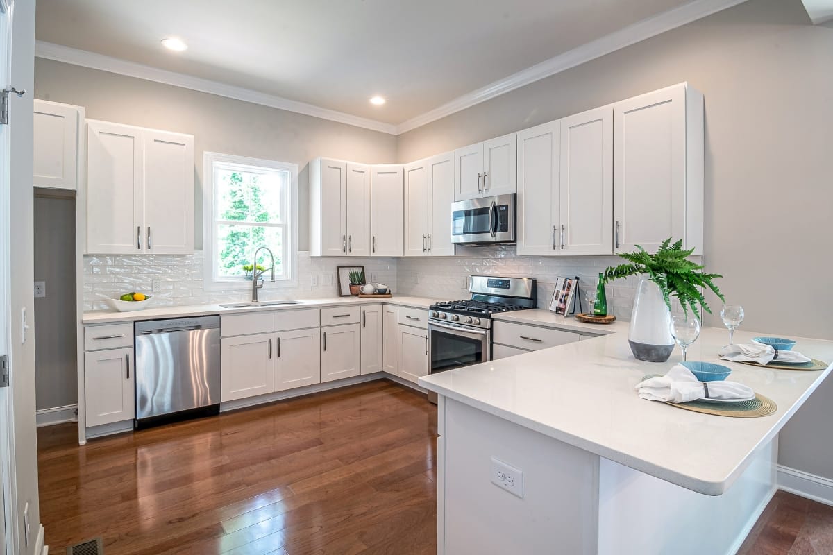 Affordable Kitchen Upgrades: Budget Remodeling Ideas for Smyrna Homes 3 Modern kitchen with white cabinets, stainless steel appliances, wooden floors, a large window above the sink, and a peninsula set for dining—perfect for showcasing affordable kitchen upgrades.
