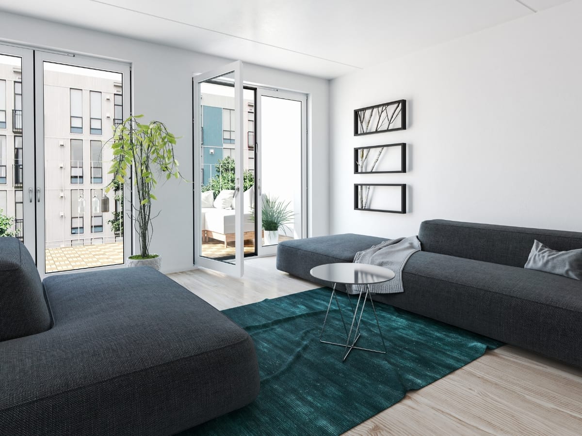 Atlanta-Midtown Condo Remodeling Tips: How to Maximize Small Spaces with Smart Design 11 Modern living room showcases dark gray sofas, a round coffee table, green rug, wall art, a potted plant, and glass doors leading to a balcony with city views—perfect for stylish condo remodeling.