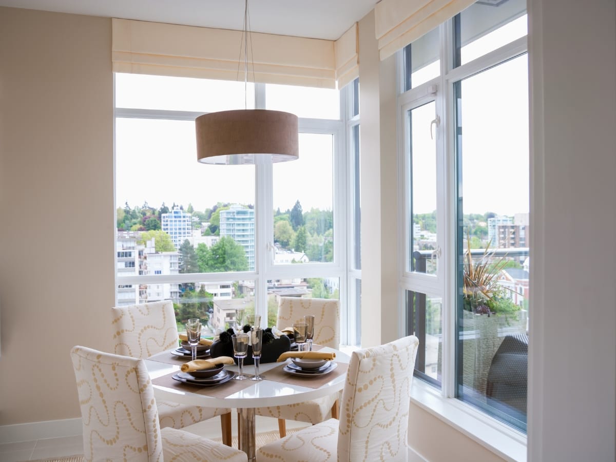 Atlanta-Midtown Condo Remodeling Tips: How to Maximize Small Spaces with Smart Design 12 A round dining table set for four sits by large windows in a bright, modern apartment with a city view, showcasing elegant condo remodeling.