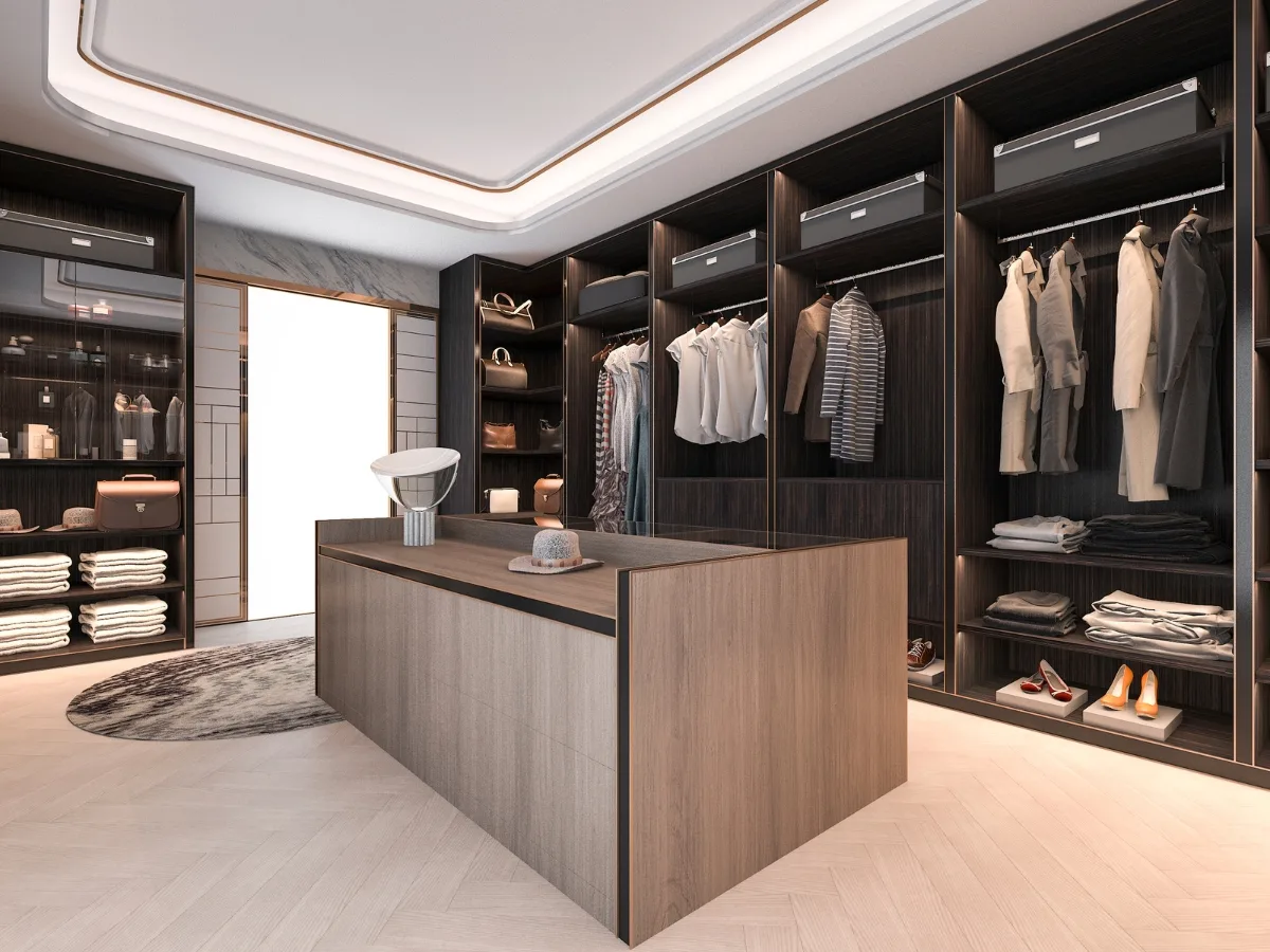 Modern walk-in closet with dark wood open shelving, neatly organized clothes, shoes, and accessories&mdash;expertly crafted by custom closet designers&mdash;featuring a central island and a white chair on a round rug.