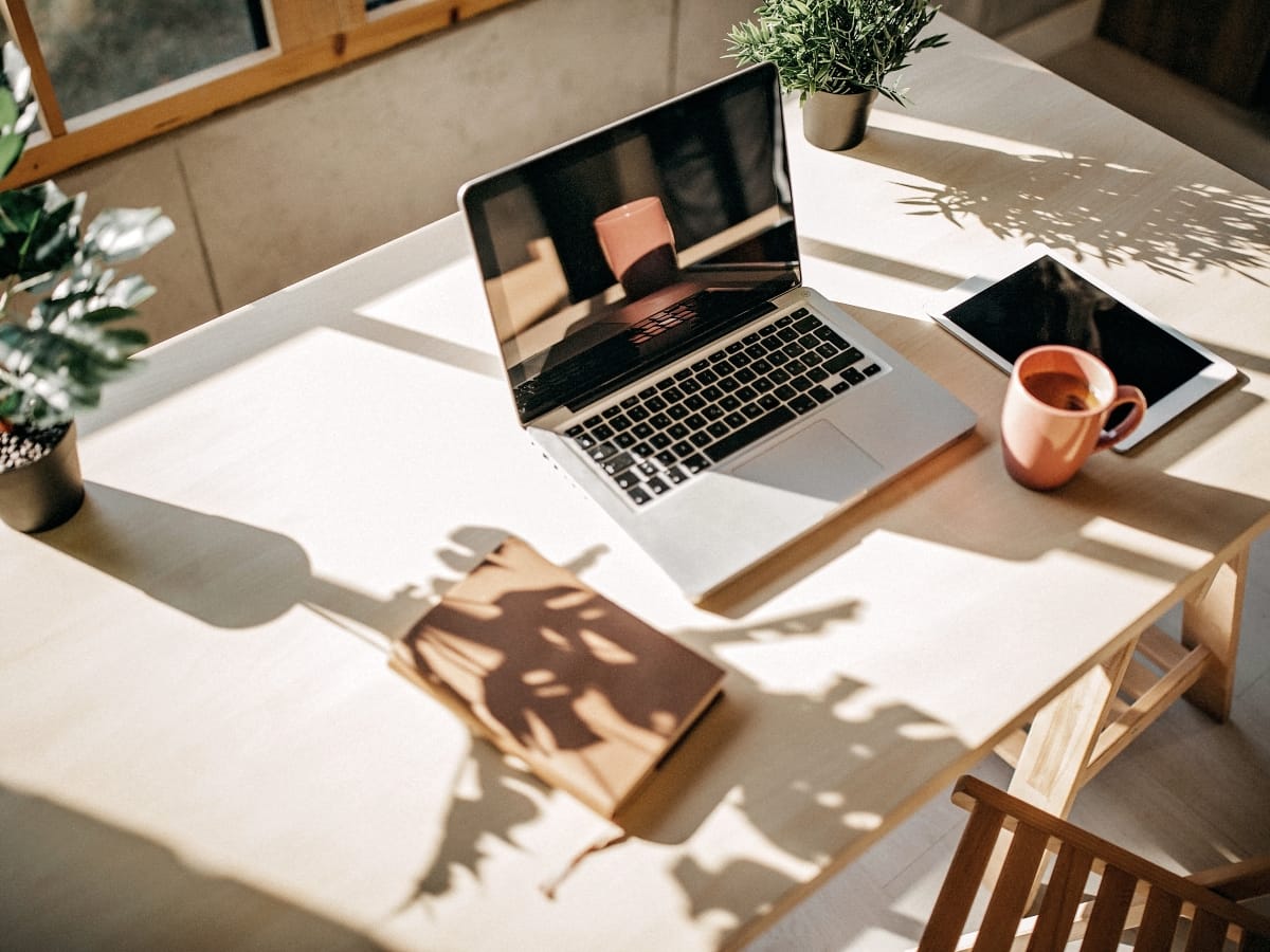 Brookhaven GA Home Office Remodeling Ideas for a Productive Workspace 3 A laptop, notebook, coffee mug, tablet, and potted plants sit on a sunlit wooden desk near a window—perfect inspiration for your next home office remodeling.