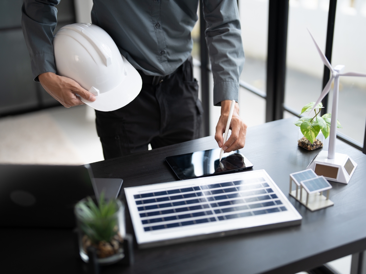 Johns Creek Energy-Efficient Home Remodeling: The Best Green Upgrades for Long-Term Savings 3 A person in Johns Creek holds a white hard hat and uses a tablet at a desk with solar and wind turbine models, planning green upgrades and energy-efficient home remodeling.