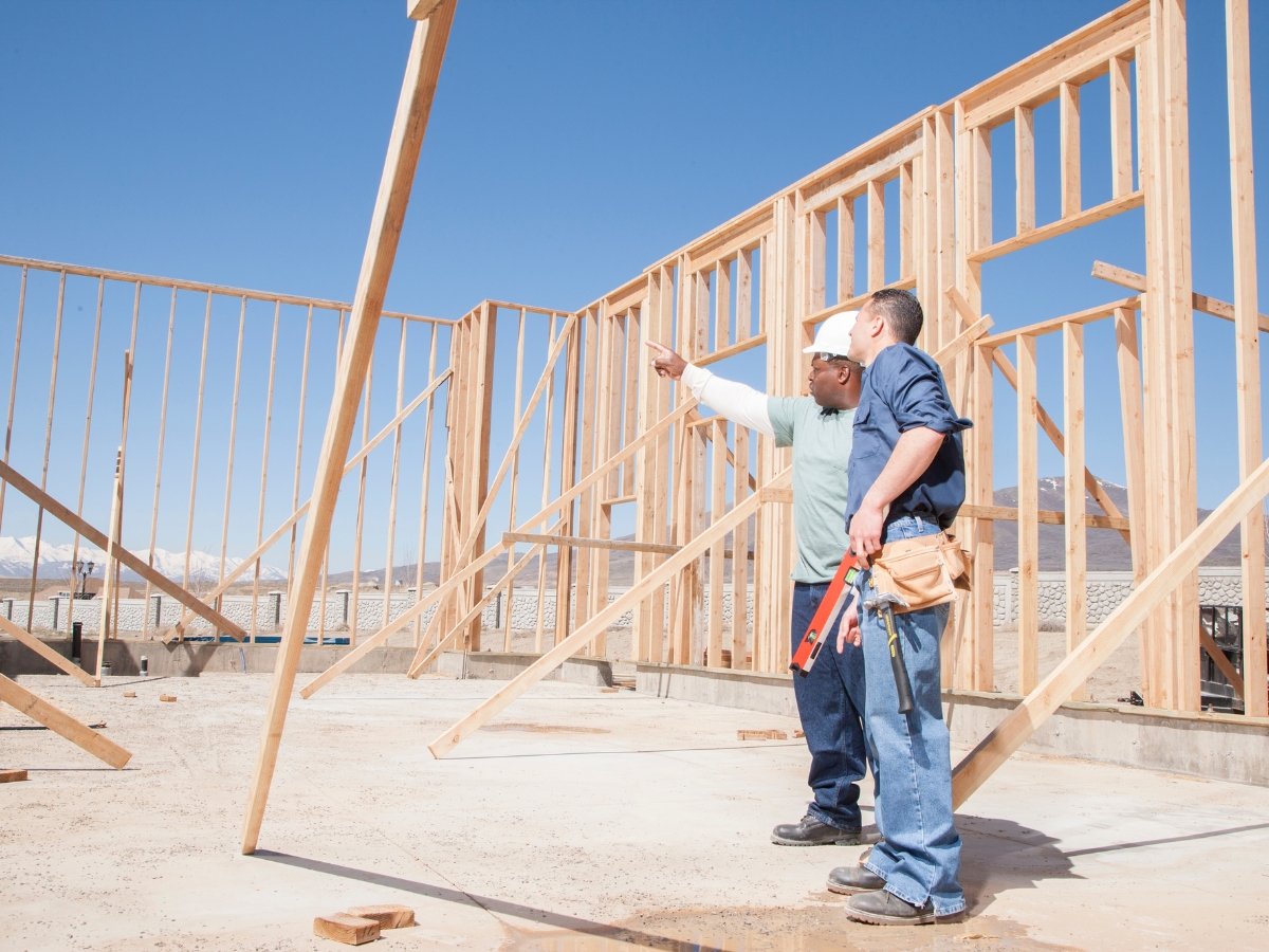Kennesaw Exterior Home Remodeling: Top Curb Appeal Enhancements That Boost Property Value 5 Two construction workers discuss and review the wooden framing of a building under construction at a worksite, considering how their craftsmanship will boost property value on a clear day.