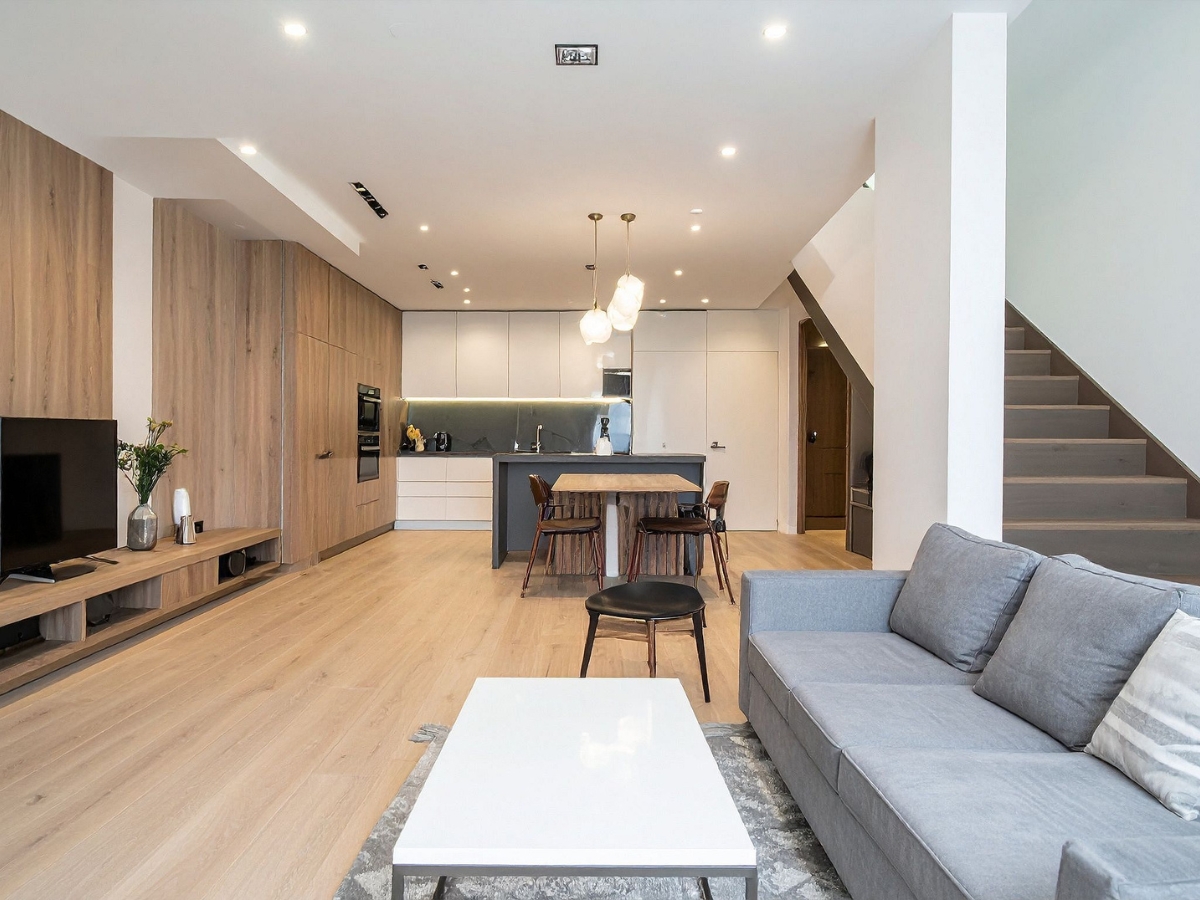 Modern open-plan living space with a gray sofa, white coffee table, flat-screen TV, wood floors, and a kitchen featuring pendant lights, island seating for entertaining guests, and elegant wooden cabinetry—ideal for Marietta kitchen remodeling.