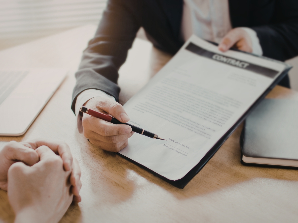 A General Contractor Checklist for Hiring the Right Professional For the Job 7 A person in business attire points to a contractor checklist with a pen while another person listens, both seated at a desk with documents.