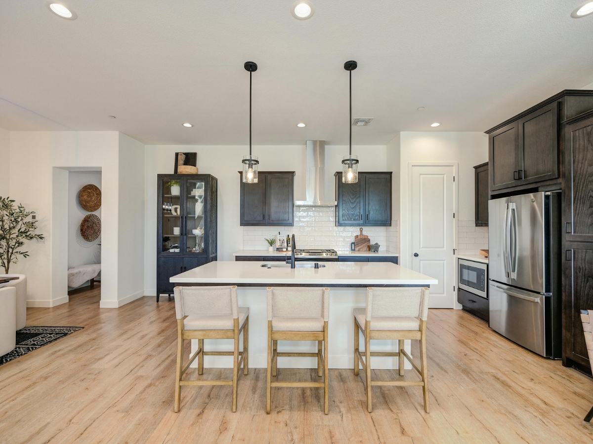 Essential Kitchen Lighting Design for Atlanta Homes 4 Modern kitchen with a large island, three beige chairs, stainless steel appliances, dark wood cabinets, and stylish kitchen lighting with pendant fixtures over the island.