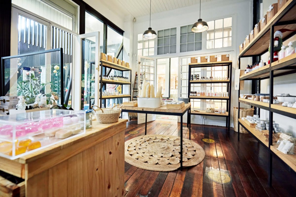About Us 42 A well-lit shop interior with wooden shelves and tables displaying various soaps, bottles, and jars; large windows fill the space with light, while a rug rests on the polished wooden floor, creating an inviting atmosphere all about natural beauty.