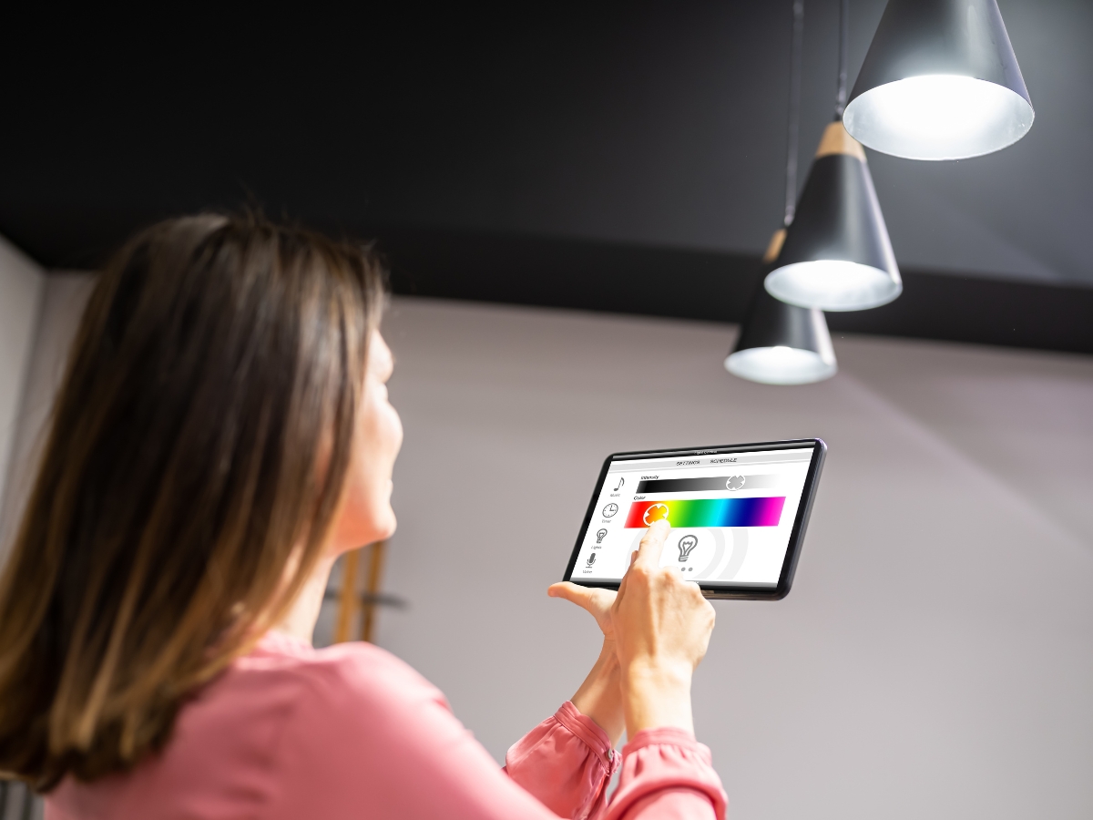 A woman uses a tablet to control Smart Lighting, effortlessly adjusting color and brightness settings for her ceiling lights.