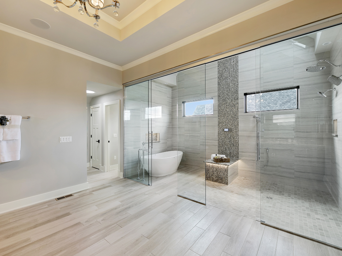 Spacious modern bathroom with a sleek walk-in shower, freestanding bathtub, light wood flooring, tile accents, and recessed lighting.