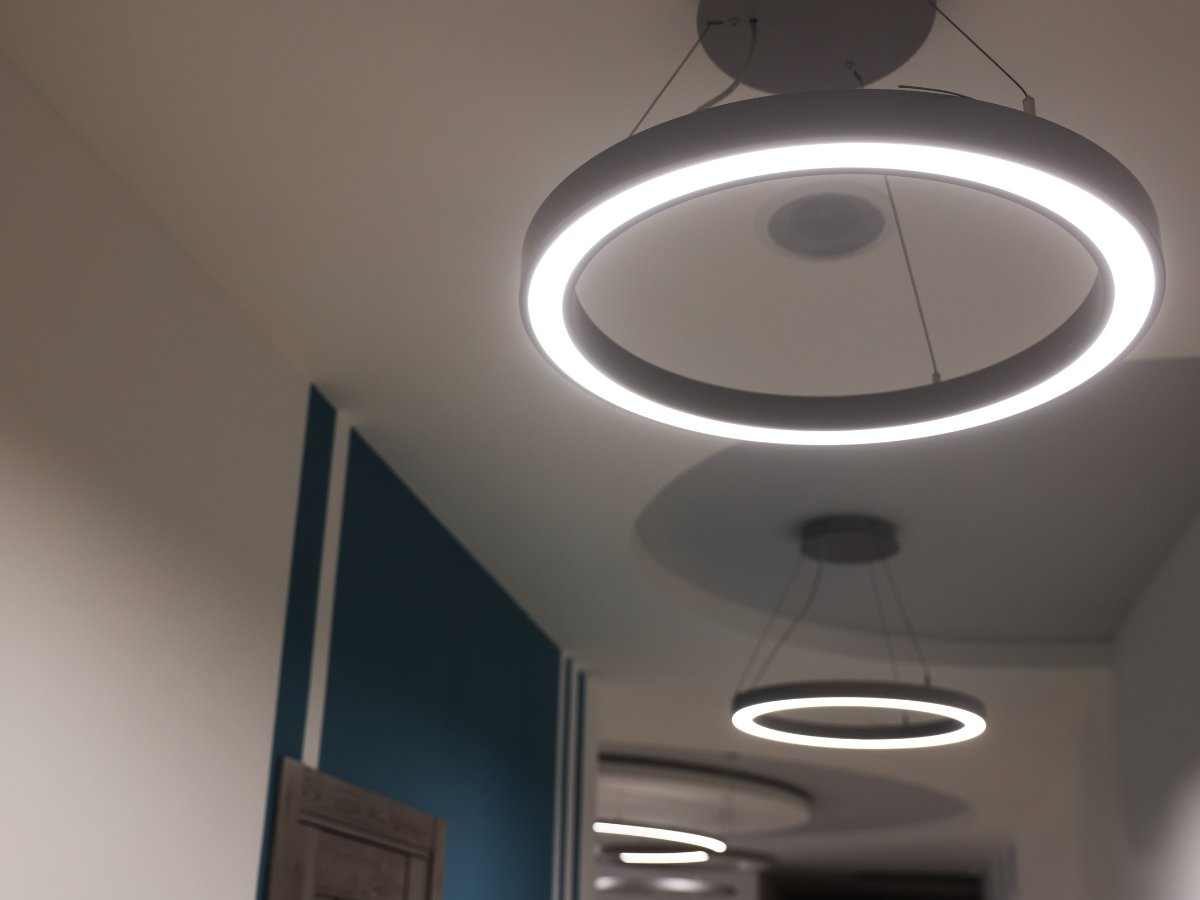 Effective Lighting Design for Home Remodeling 2 Two circular pendant lights with LED rings hang from the ceiling in a hallway with white walls and a blue accent wall, showcasing modern lighting design.