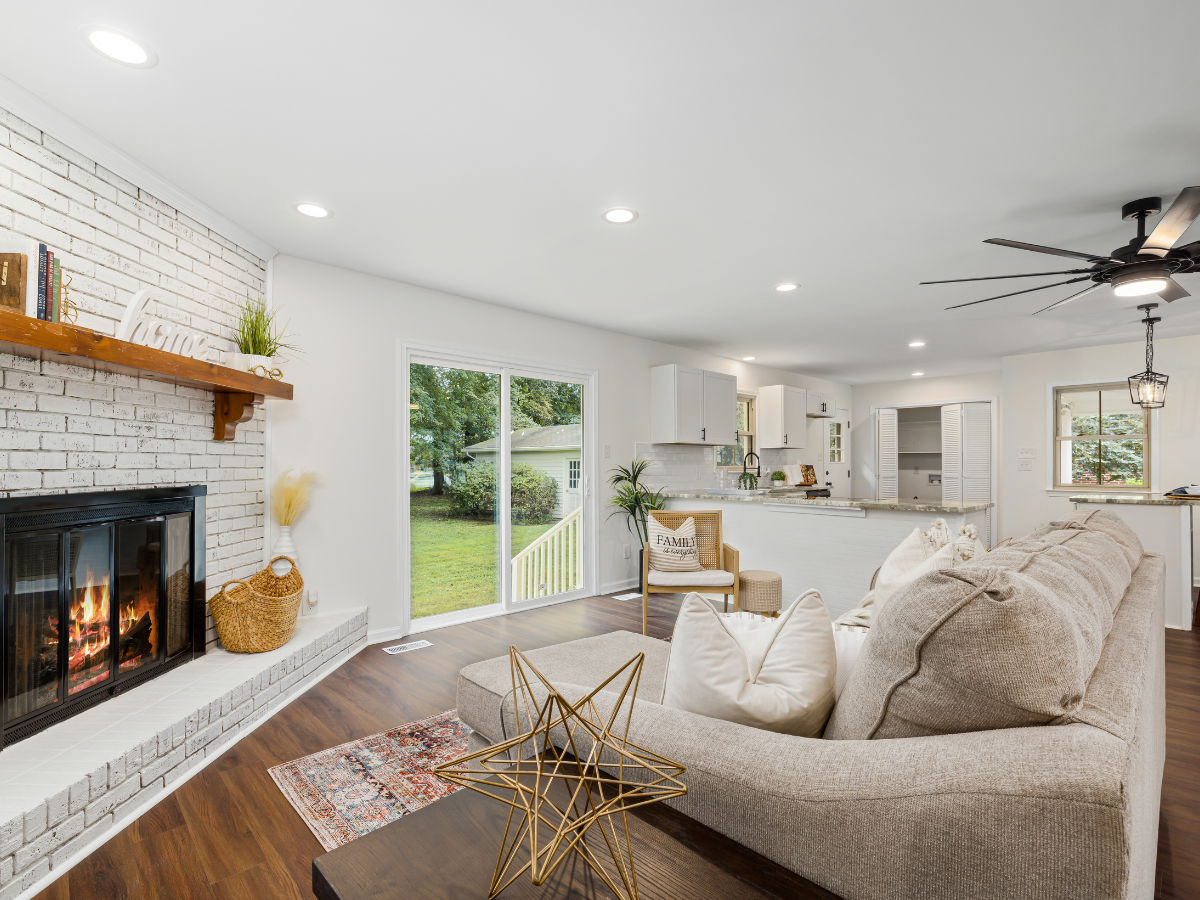 Effective Lighting Design for Home Remodeling 6 Bright living room with a beige sectional sofa, fireplace, decorative accents, and thoughtfully planned lighting design; sliding glass doors lead to a grassy backyard, with the open kitchen visible in the background.