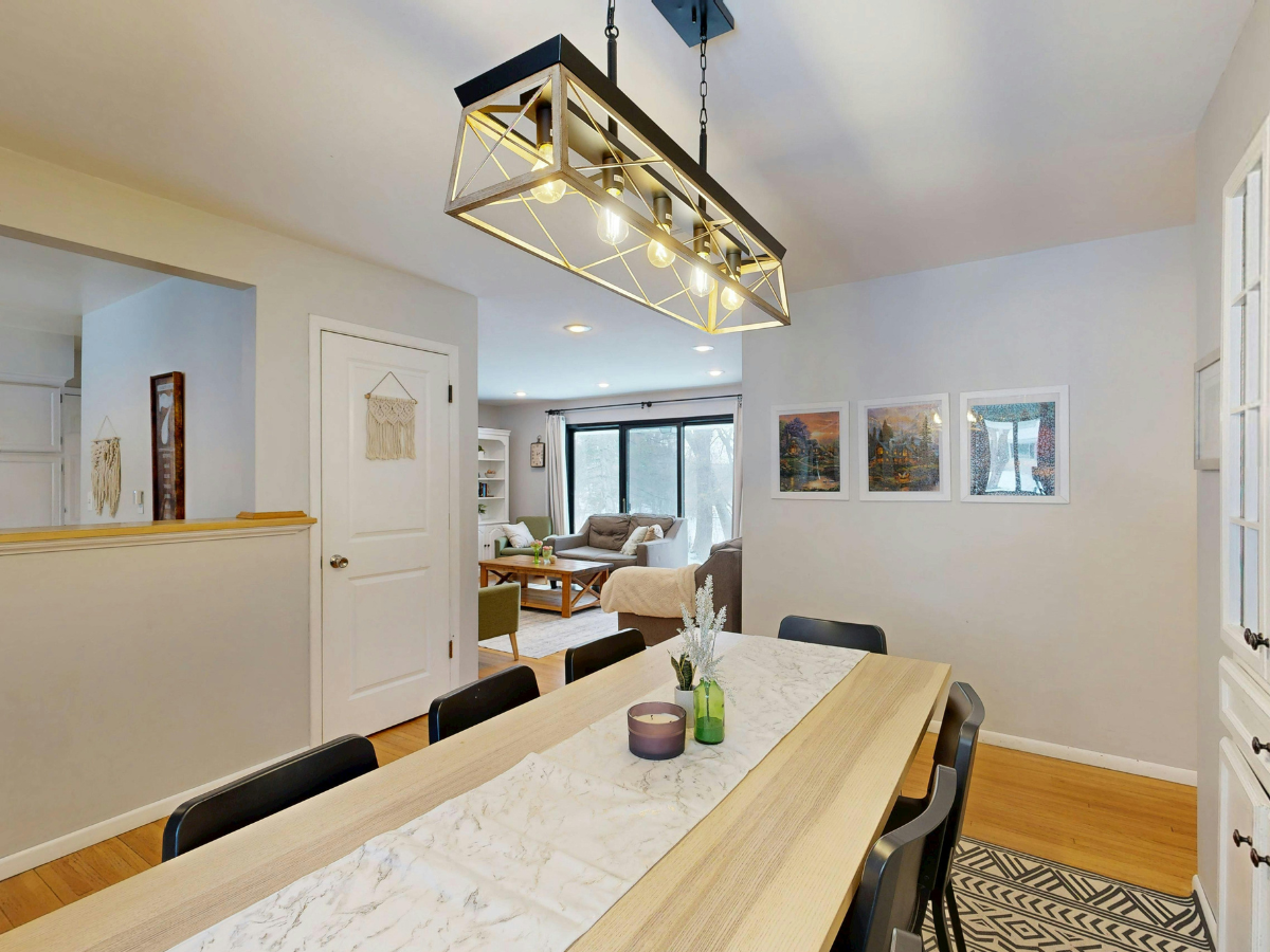 Effective Lighting Design for Home Remodeling 7 Modern dining room with a light wood table, black chairs, and a geometric chandelier showcasing elegant lighting design; living area with sofa and large windows visible in the background.