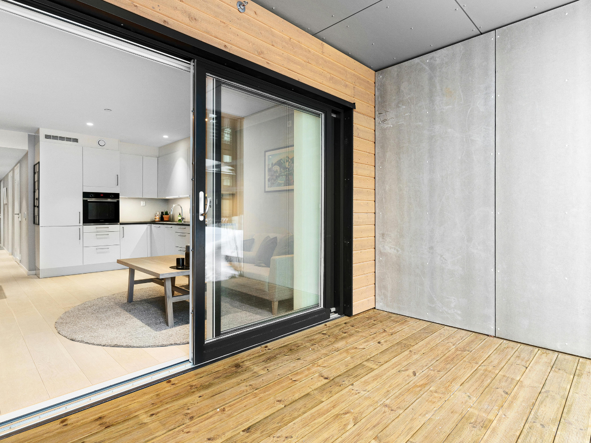 Open sliding glass door, one of the most popular door types, leads from a wooden patio into a modern living area with a gray rug, coffee table, and white kitchen cabinetry.