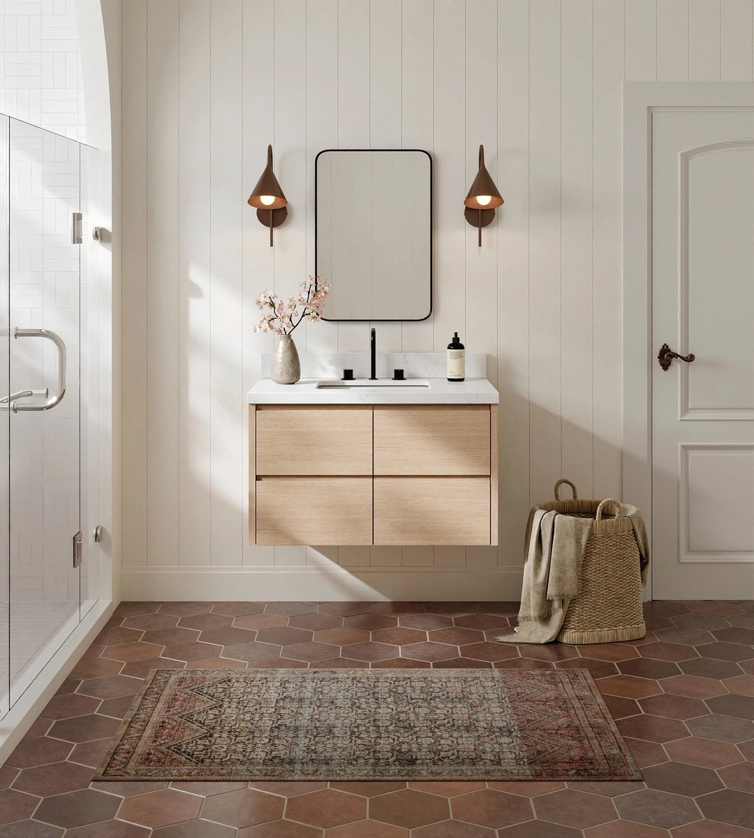 Modern bathroom renovation with a floating wood vanity, rectangular mirror, two wall sconces, a patterned rug, and a basket with towels on a hexagonal tile floor—perfect inspiration for your next office bathroom remodel.