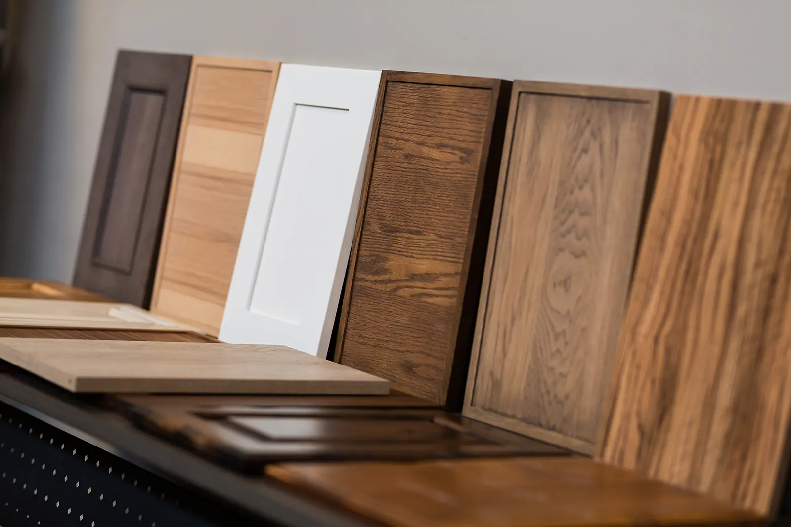 A row of DeWils Cabinets door samples in various wood finishes and a white finish, displayed upright on a counter against a neutral wall—a perfect inspiration for your next bathroom renovation or office bathroom remodel.