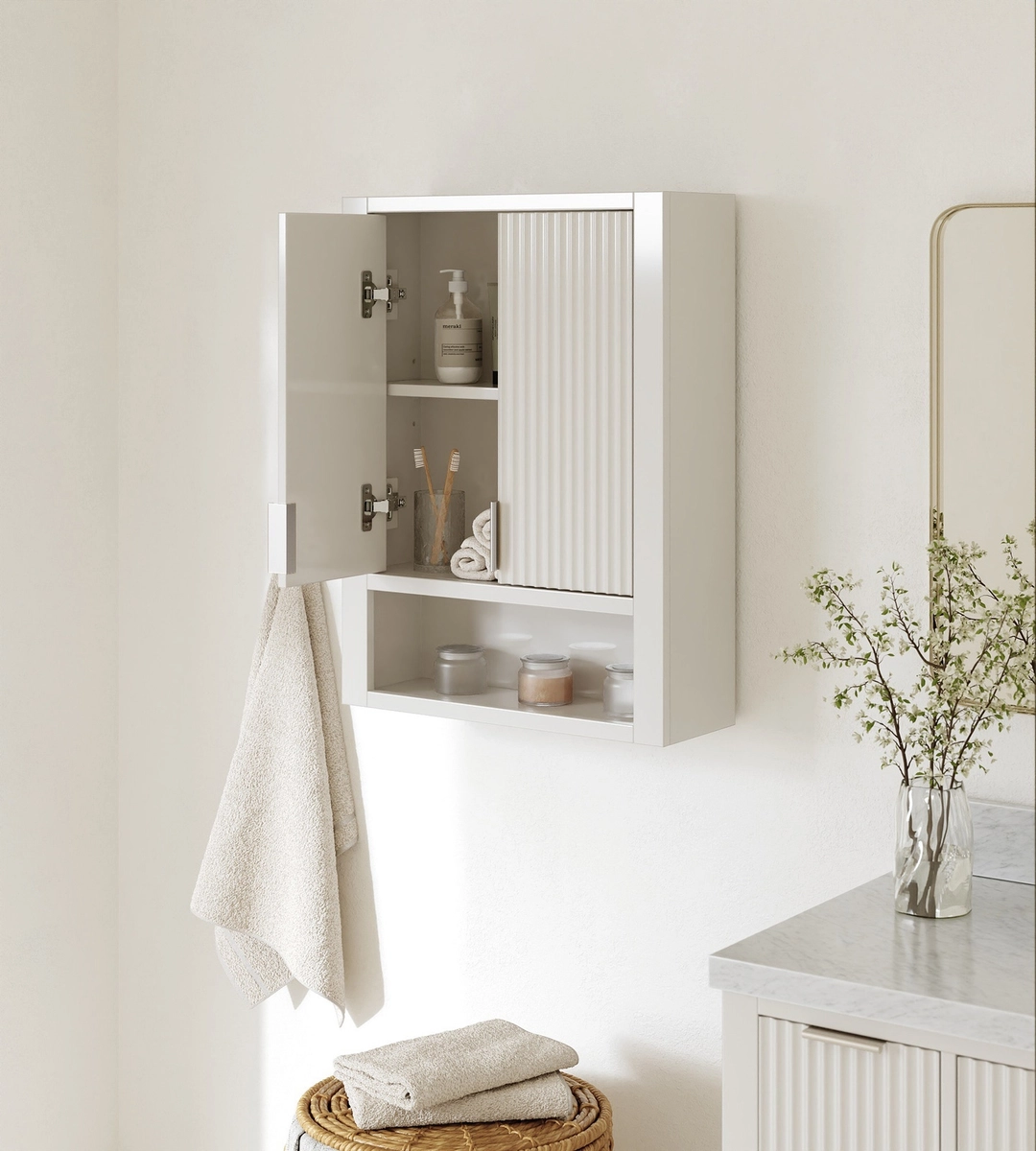 White bathroom cabinet with one door open, showing toiletries and towels inside; a towel hangs from a hook below—an inviting detail perfect for your office restroom transformation. Countertop with a vase and folded towels nearby highlights how ARIEL bathroom vanities and storage can elevate any office bathroom remodel.