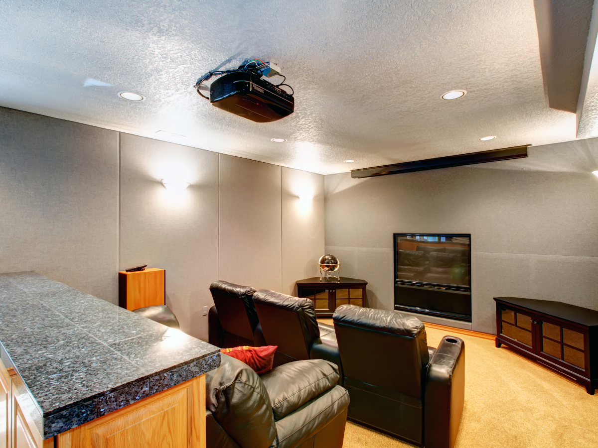 Home theater room with black leather recliners facing a flat-screen TV, a ceiling-mounted projector, and a granite countertop bar on the side—perfectly situated in a basement with waterproofing to ensure lasting comfort and protection.