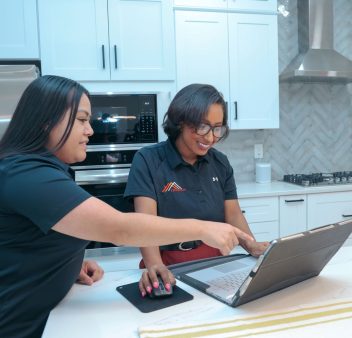 Two women working on a laptop in a kitchen.