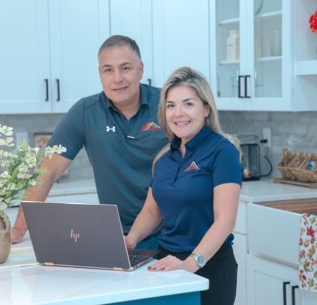 A man and woman standing in front of a kitchen with a laptop.